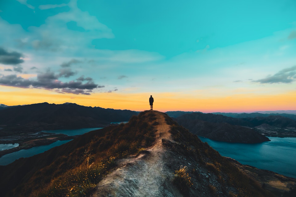 Man standing on edge of cliff at sunrise.