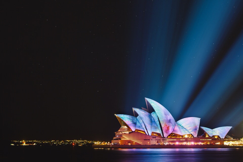 Sydney Opera House at night with multicoloured lights illuminating the exterior.