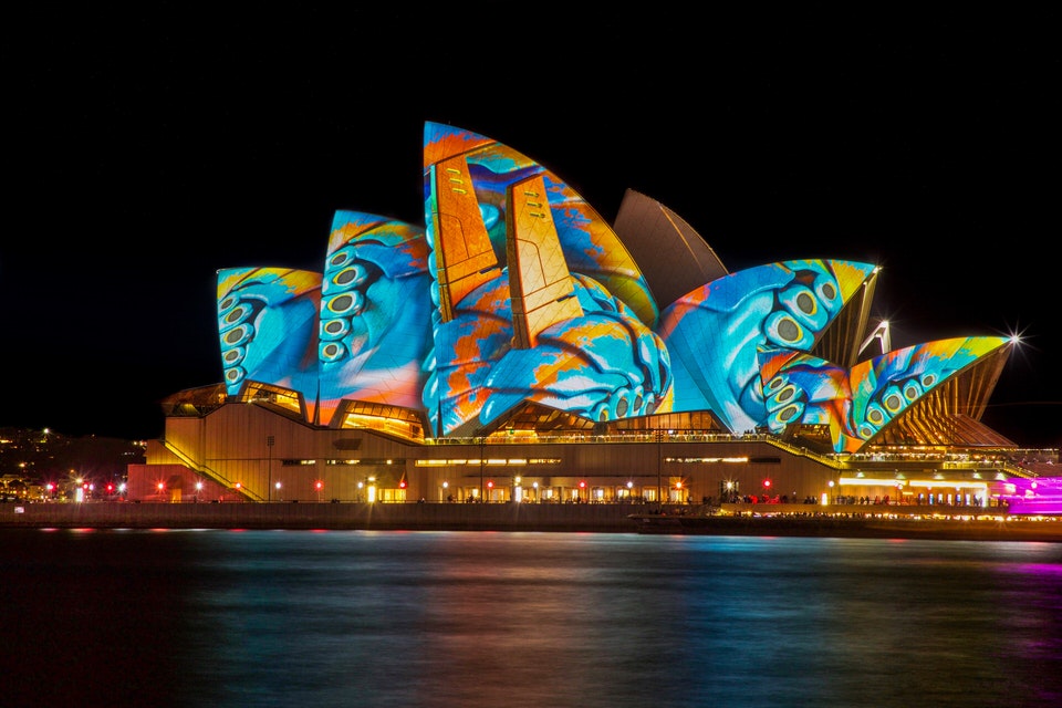 Sydney Opera House at night with multicoloured lights illuminating the exterior.