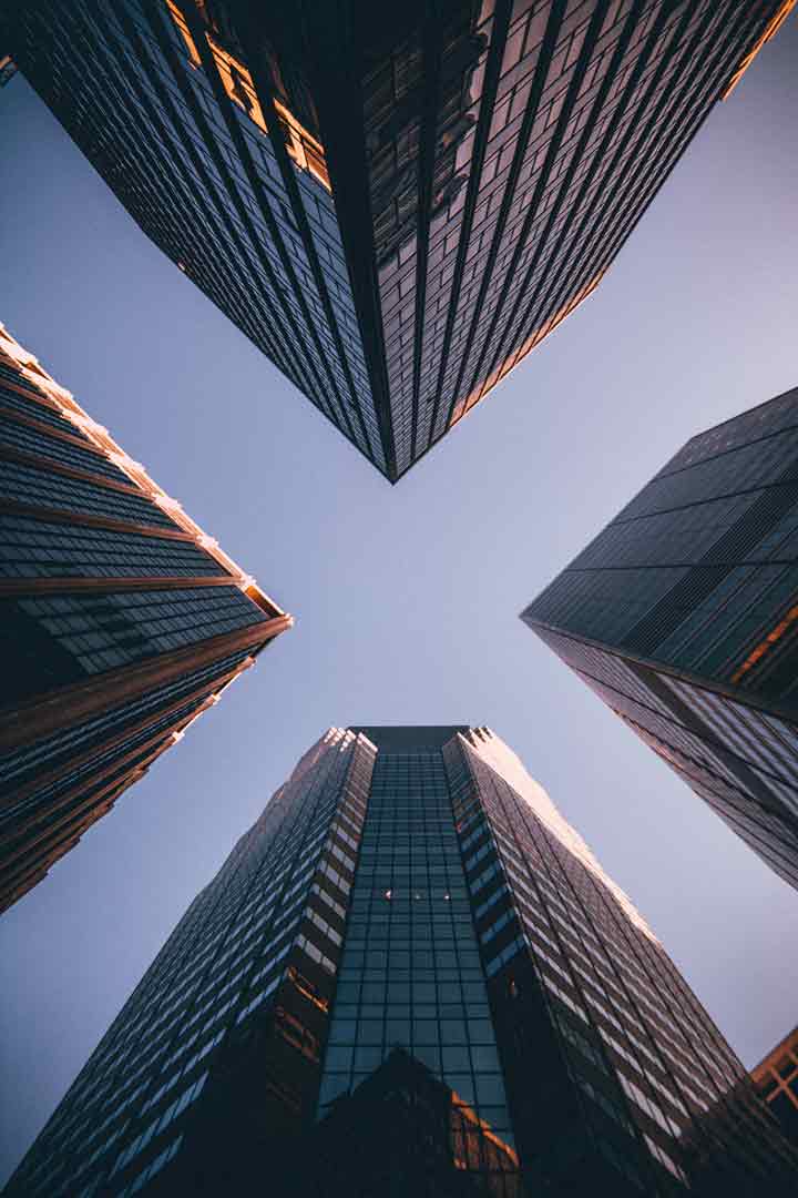 Looking up at a cross section of four buildings that form an 'X' in the skyline above. 